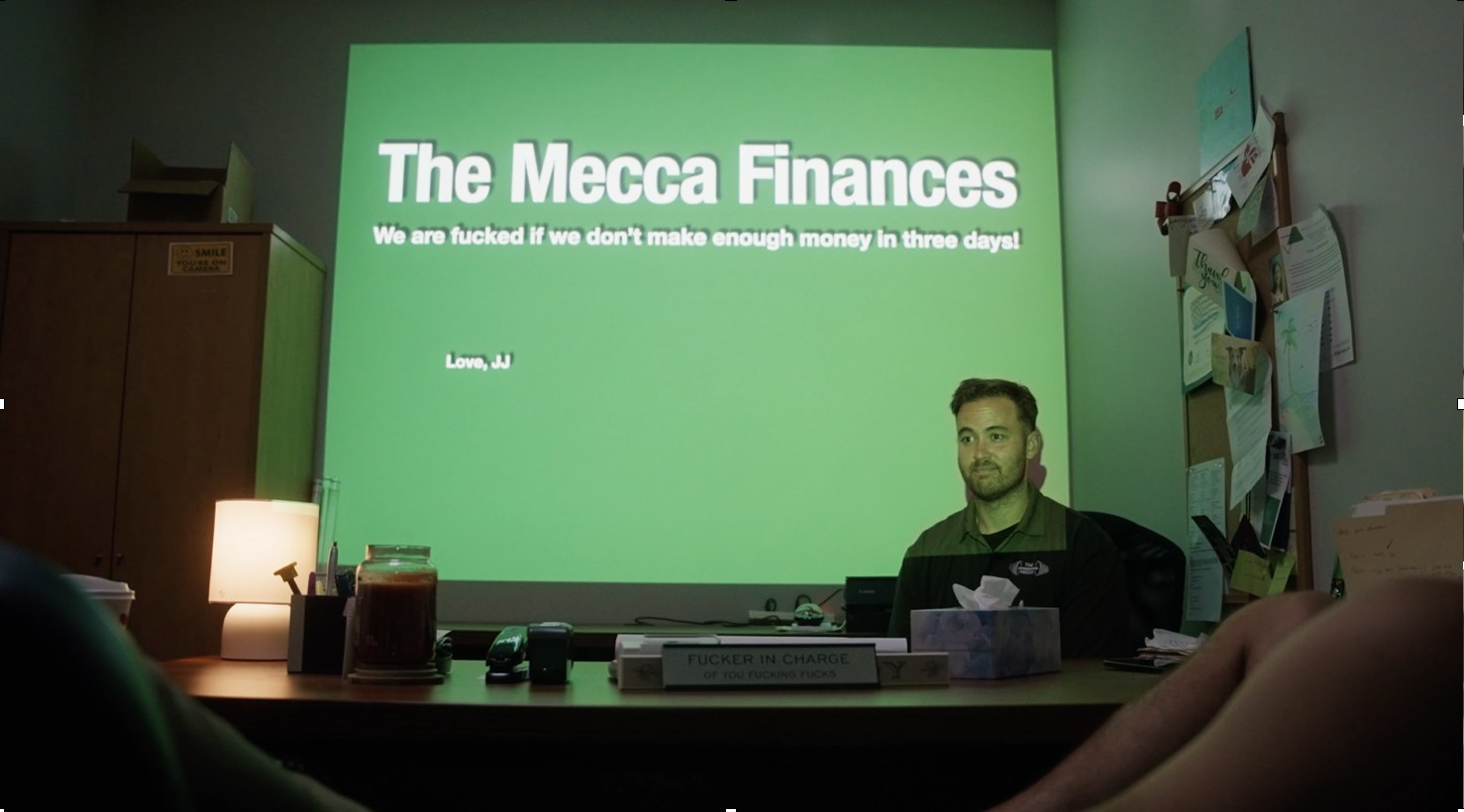 J.J. at his desk in front of a slide titled The Mecca Finances
